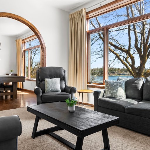 Living room with floor-to-ceiling lake view — two sofas, dining and clock visible through the archway.