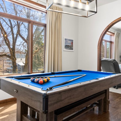 Pool table in the loft — wide bay window over downtown Charlevoix, framed by an arched walnut passthrough.