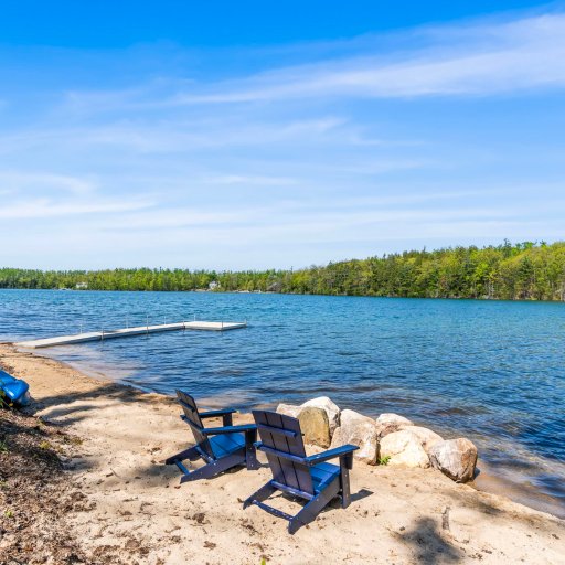 Sandy beach with Adirondack chairs, kayaks, and dock